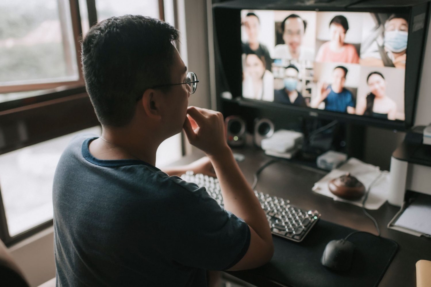 an asian chinese mid adult man talking and communicating with his friends and business partners online chatting looking at camera discussion from a computer monitor screen at home office